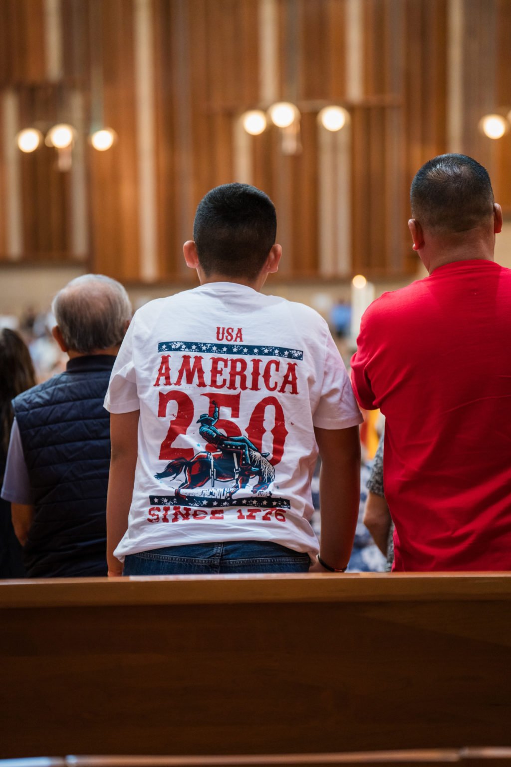 Un feligrés viste una camiseta con el lema "America 250" durante la Misa por la Nación, celebrada el 3 de julio en la Catedral de Nuestra Señora de los Ángeles. (Isabel Cacho)