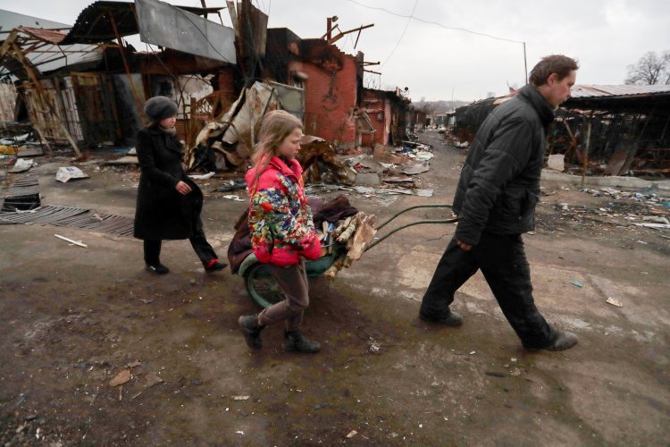 Un hombre tira de un carro de madera junto a una mujer y una niña mientras pasan por edificios destruidos en la ciudad portuaria de Mariupol, Ucrania, el 14 de abril de 2022, durante la guerra de Rusia. (Foto CNS photo/Alexander Ermochenko, Reuters)