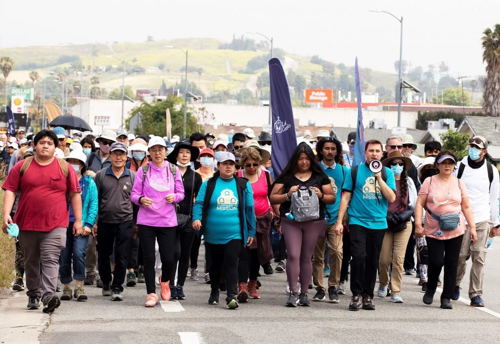 Los peregrinos rezan el rosario mientras caminan por el Eastside de Los Ángeles de camino a la Catedral de Nuestra Señora de los Ángeles durante la peregrinación jubilar "Camino" el 2 de abril de 2022. El padre Parker Sandoval sostiene el altavoz. (Foto Víctor Alemán)