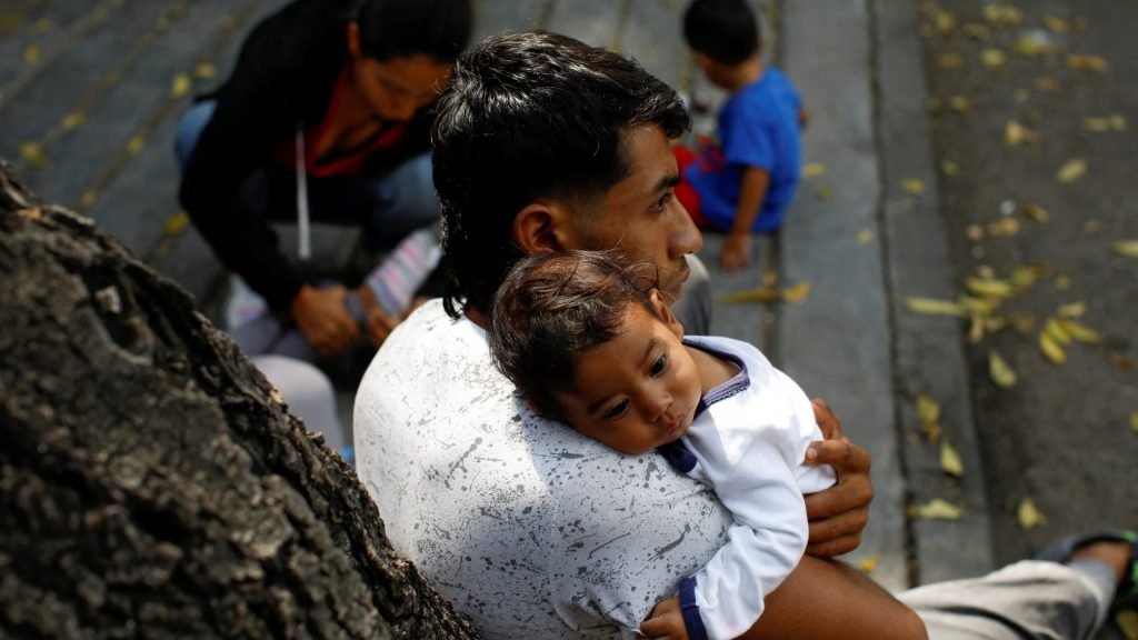 Un migrante venezolano en Ciudad de México sostiene a su bebé el 27 de octubre de 2022, mientras espera en la acera con su familia fuera de la Comisión Mexicana de Ayuda a los Refugiados. (CNS /Raquel Cunha, Reuters)