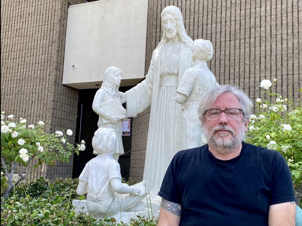 Michael Stucchi posa delante de la estatua restaurada de Jesús con niños en la iglesia de San Mel en Woodland Hills. (Tom Hoffarth)