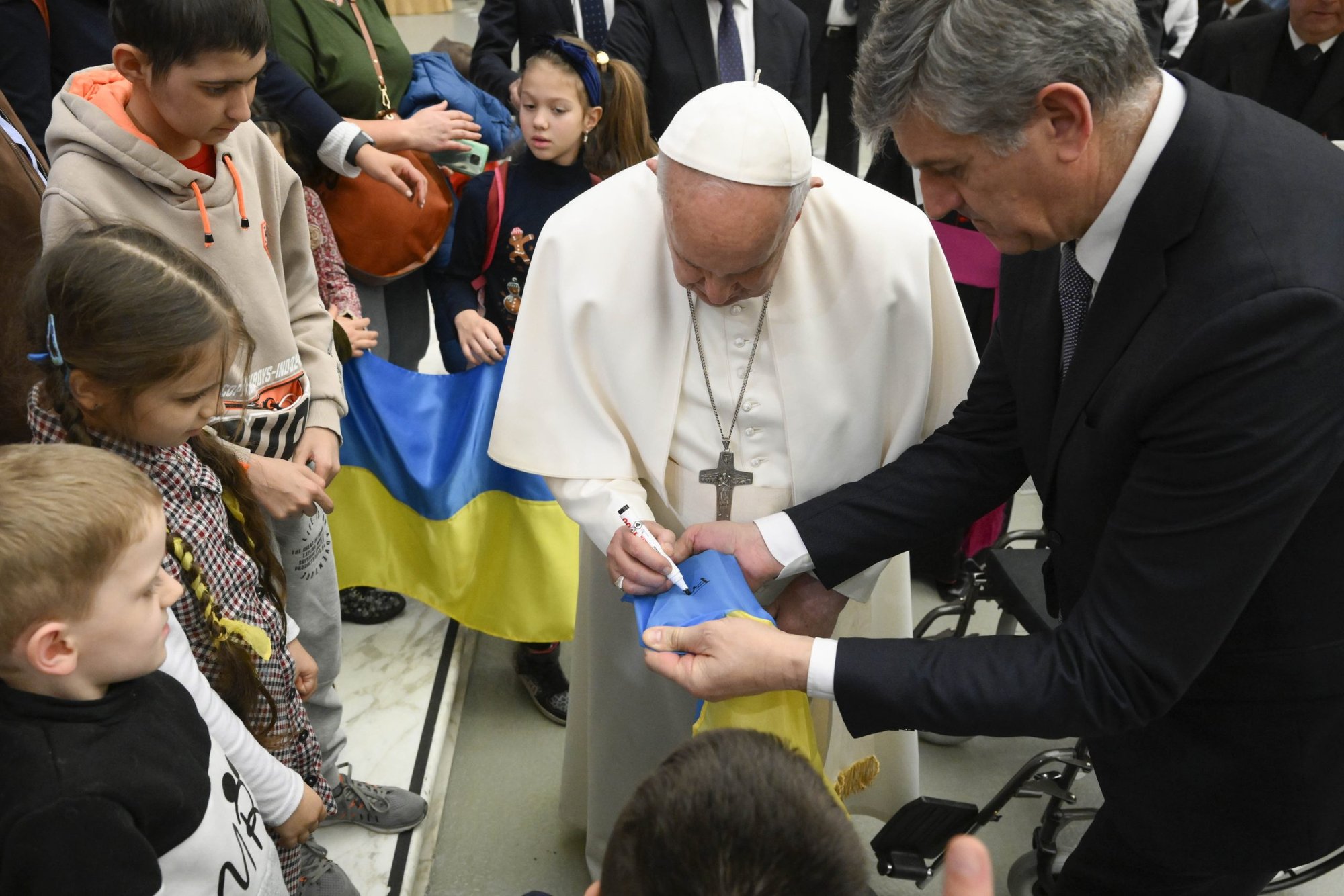 El Papa Francisco firma una bandera ucraniana para un niño ucraniano al final de su audiencia general semanal del 22 de febrero de 2023, en la sala de audiencias del Vaticano. Durante la audiencia, el Papa señaló que el aniversario de la invasión rusa de Ucrania es el 24 de febrero y rezó por el fin de la guerra. (CNS/Vatican Media