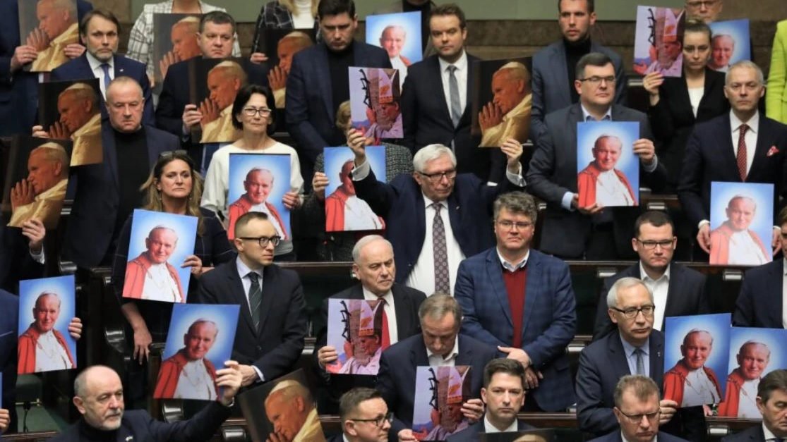 Polish lawmakers display images of St. John Paul II during a parliamentary debate over recent media reports on the late pope’s record on sexual abuse cases. (Screen capture via Crux)