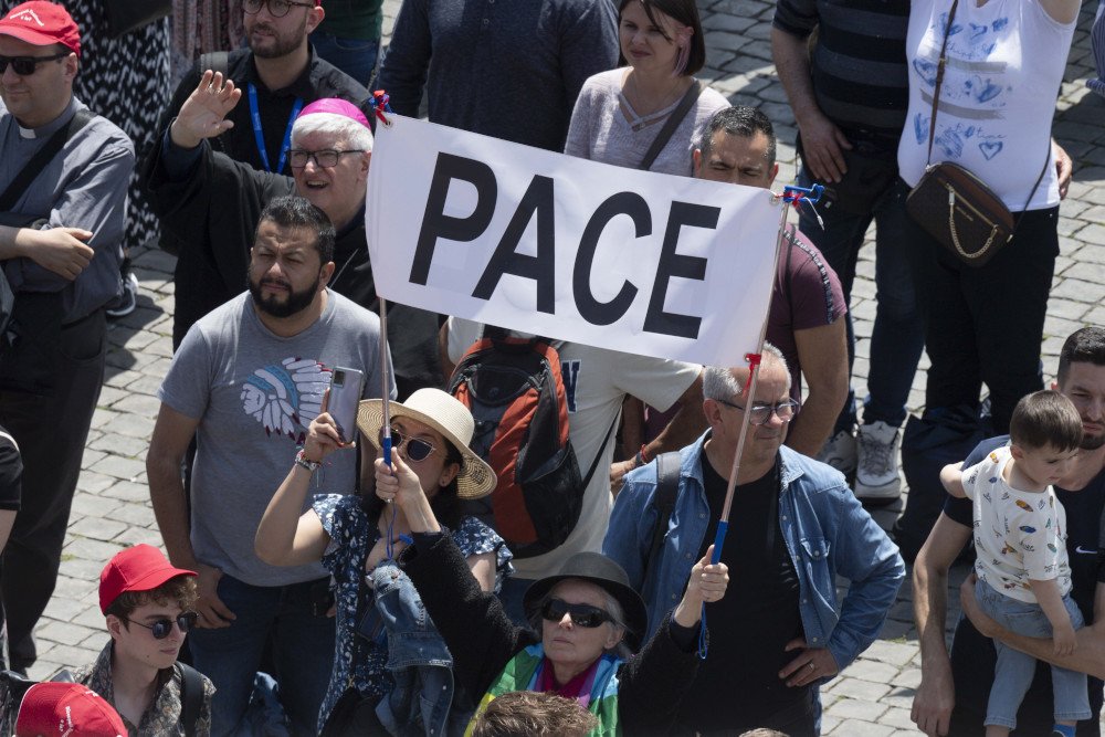 Unas personas sostienen un cartel que dice "Paz", mientras se unen al Papa Francisco para el rezo del mediodía de la oración "Regina Coeli" en la Plaza de San Pedro en el Vaticano el 21 de mayo de 2023. (CNS /Vatican Media)