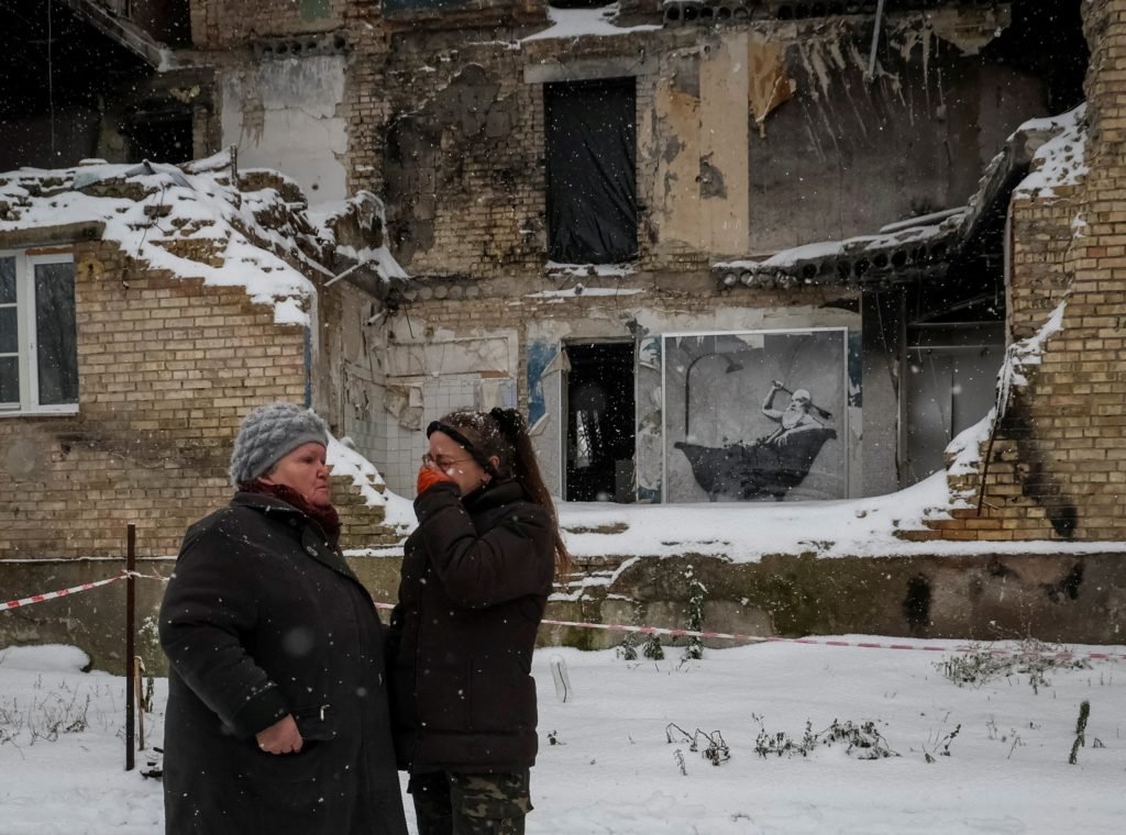 Local resident Tetiana Reznychenko cries as she speaks with her neighbor, near a work of world-renowned graffiti artist Banksy, at the wall of destroyed building in the Ukrainian village of Horenka, Nov. 19, 2022. (CNS photo/Gleb Garanich, Reuters)