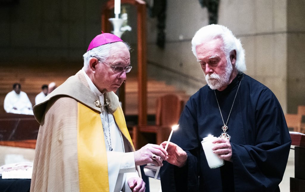 El reverendo Alexei Smith, responsable interreligioso de la archidiócesis, ayuda al arzobispo José H. Gómez a encender una vela en recuerdo de las personas sin hogar que han muerto en las calles de Los Ángeles, en la catedral de Nuestra Señora de los Ángeles, el 21 de diciembre de 2023. Smith es párroco de la iglesia greco-católica rusa de San Andrés en El Segundo. (Víctor Alemán)