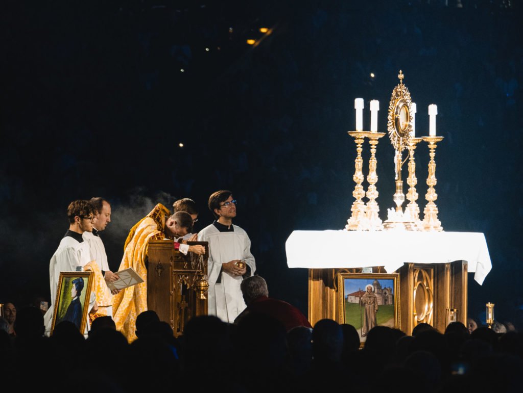 El Obispo Andrew H. Cozzens se arrodilla en oración ante la custodia durante la adoración eucarística en la sesión inaugural del Congreso Eucarístico Nacional en el Lucas Oil Stadium de Indianápolis el 17 de julio. El altar estaba adornado con los iconos de los santos que llevaban los peregrinos perpetuos de la peregrinación nacional de dos meses. (OSV News/Bob Roller)