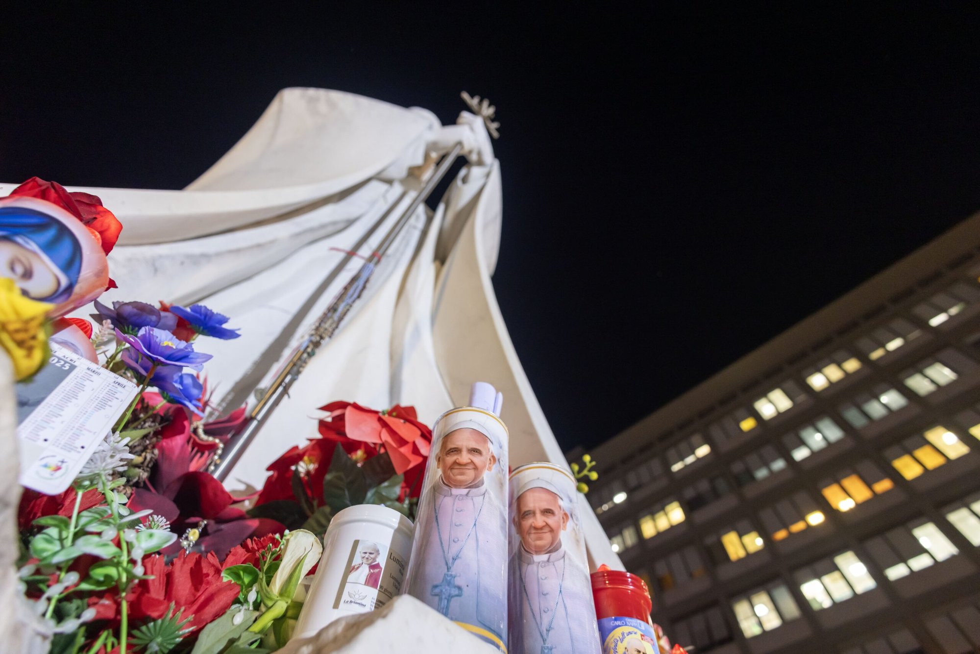 Velas votivas y flores se ven en la base de una estatua de San Juan Pablo II fuera del hospital Gemelli de Roma el 21 de febrero de 2025, donde el Papa Francisco está siendo tratado por una neumonía doble. (CNS photo/Pablo Esparza)
