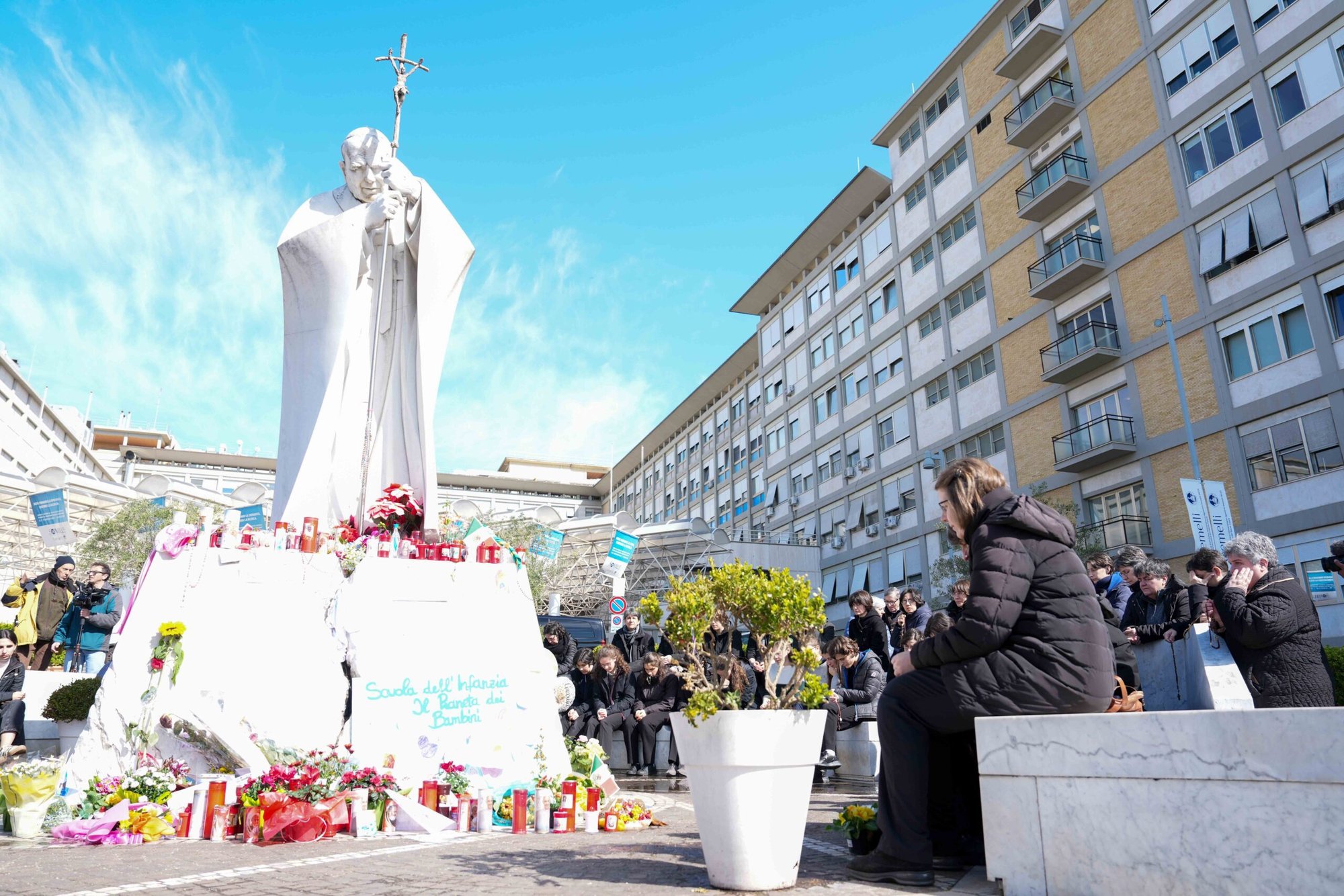 Jóvenes y miembros de la Casa de María, grupos asociados a la Pontificia Academia de la Inmaculada Concepción, y otras personas rezan alrededor de una estatua de San Juan Pablo II frente al hospital Gemelli de Roma el 2 de marzo de 2025. El Papa Francisco está recibiendo allí tratamiento para una doble neumonía. (CNS photo/Lola Gomez)