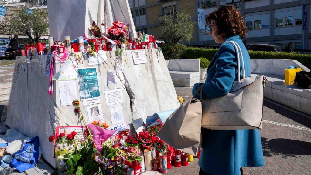 Una mujer junto a una estatua de San Juan Pablo II en el exterior del hospital Gemelli de Roma, el 6 de marzo de 2025, mirando mensajes y dibujos para el Papa Francisco, hospitalizado allí desde el 14 de febrero, recibiendo tratamiento para una neumonía doble. (CNS photo/Lola Gomez)