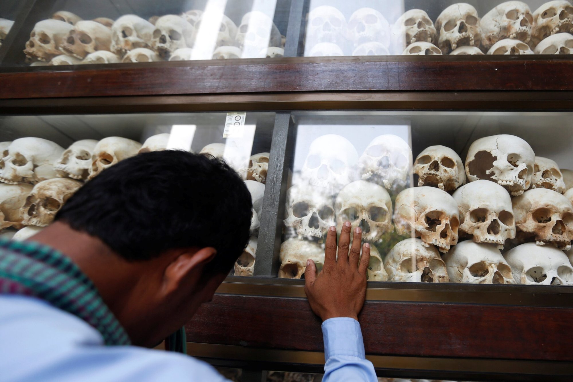 En una foto de archivo, un hombre toca una vitrina que contiene 5.000 cráneos humanos pertenecientes a las víctimas del régimen de los Jemeres Rojos en el Museo del Genocidio Tuol Sleng en Phnom Penh, Camboya. Millones de camboyanos que viven con las cicatrices de la ola de terror genocida de Pol Pot de 1975-1979 se enfrentan a la posibilidad de que el tribunal respaldado por la ONU no pueda llevar ante la justicia a los máximos responsables de la muerte de aproximadamente 1,8 millones de personas. (Foto de OSV News/Samrang Pring, Reuters)