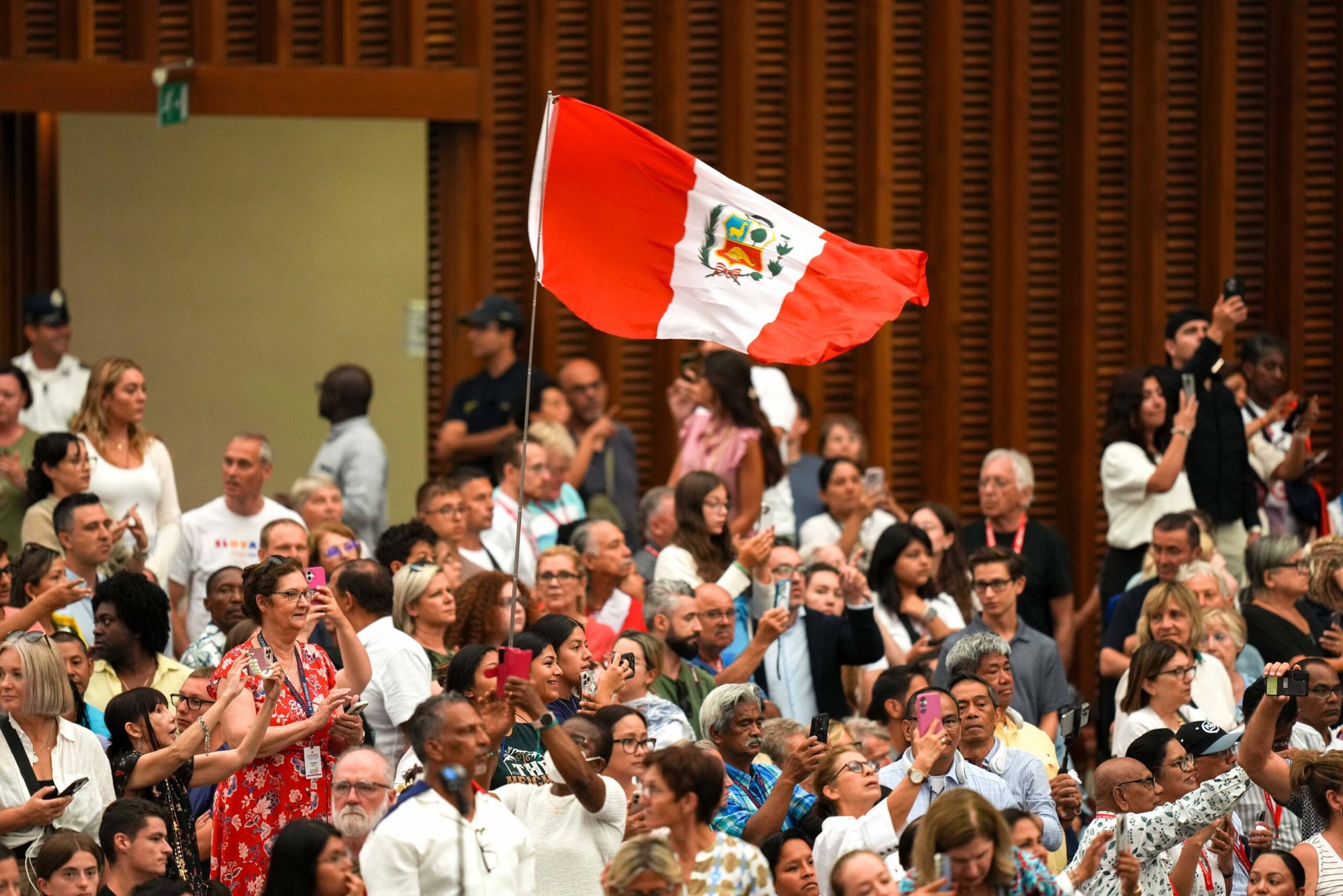 Peregrinos izan la bandera de Perú cuando el Papa León XIV llega a la Sala de Audiencias Pablo VI en el Vaticano para su audiencia general el 13 de agosto de 2025. (Foto CNS/Lola Gómez)