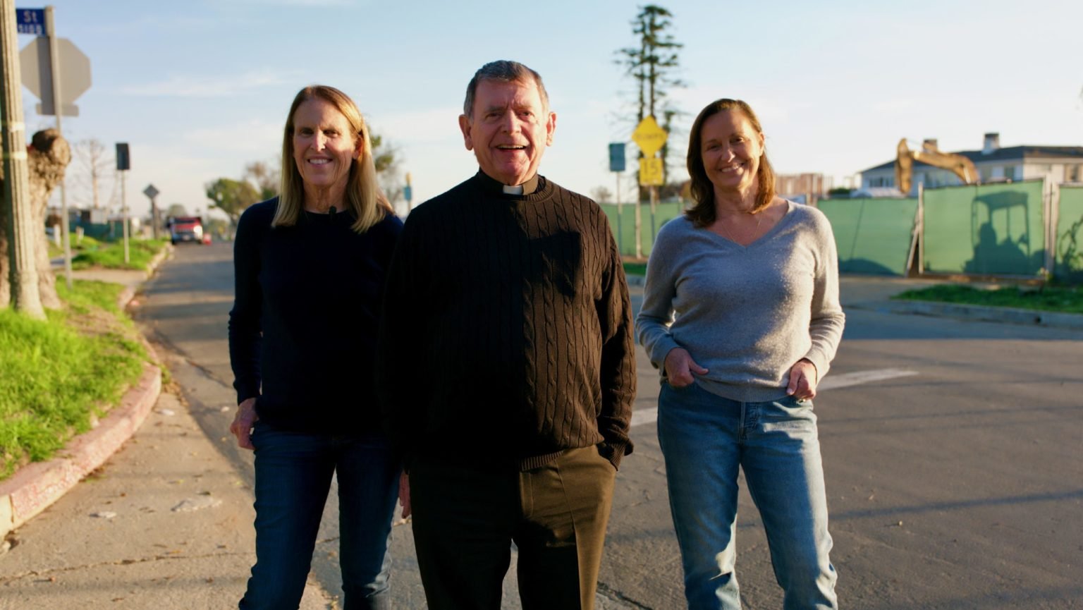 De izquierda a derecha: Sue Kohl, monseñor Liam Kidney y Paola Sessarego durante una visita al sitio de la iglesia Corpus Christi en Pacific Palisades en diciembre de 2025. Detrás de ellos se observan varias viviendas reconstruidas que están en plena obra. (Reese Cuevas)