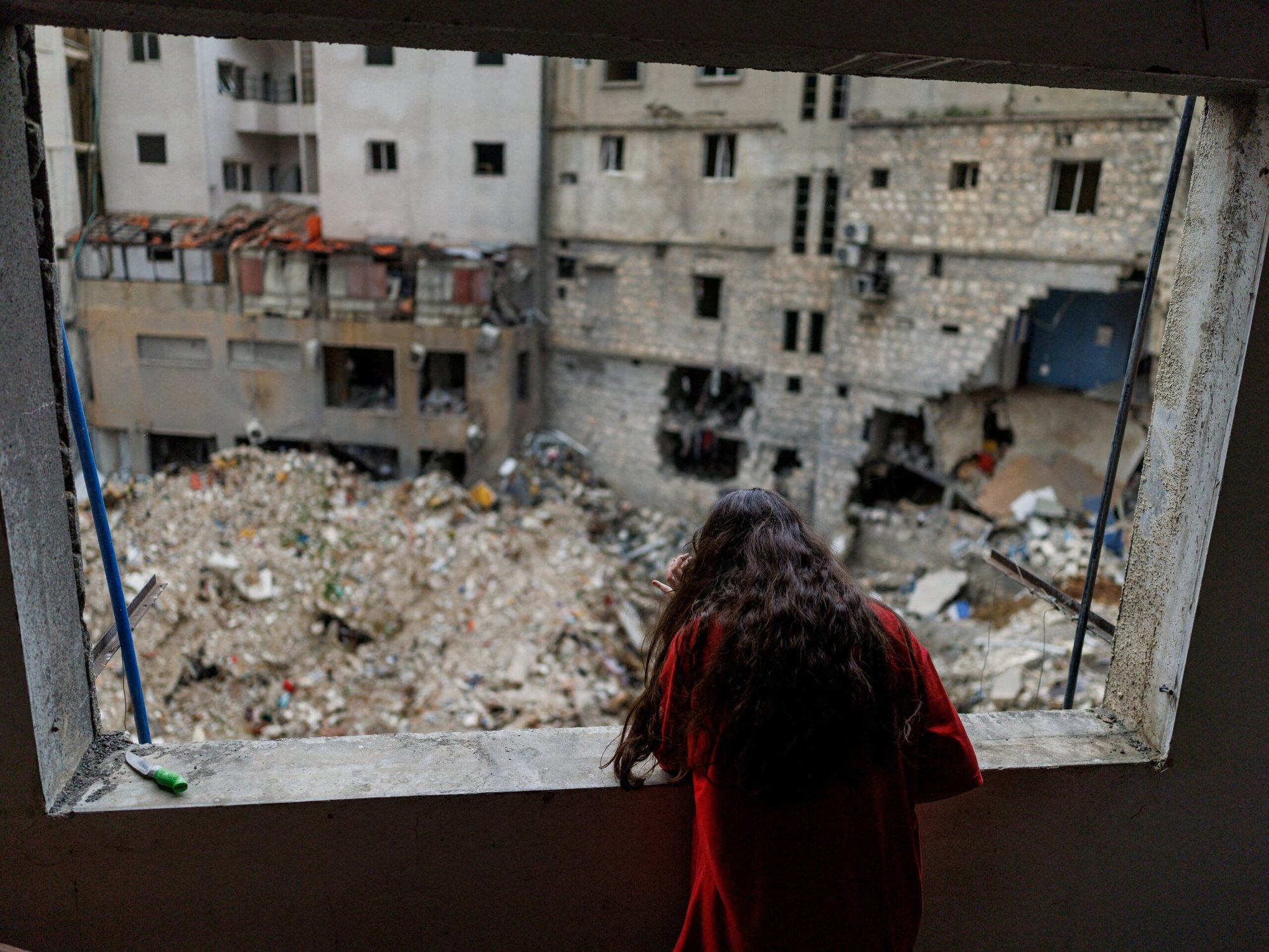 Alaa Dahnoun, de 12 años, quien dijo que sobrevivió a un ataque israelí que la obligó a huir con sus padres a Beirut, mira a través de la ventana dañada de su apartamento en Nabatieh, Líbano, el 18 de abril de 2026, después de que entrara en vigor un alto el fuego de 10 días entre Líbano e Israel. (Foto OSV News/Zohra Bensemra, Reuters)