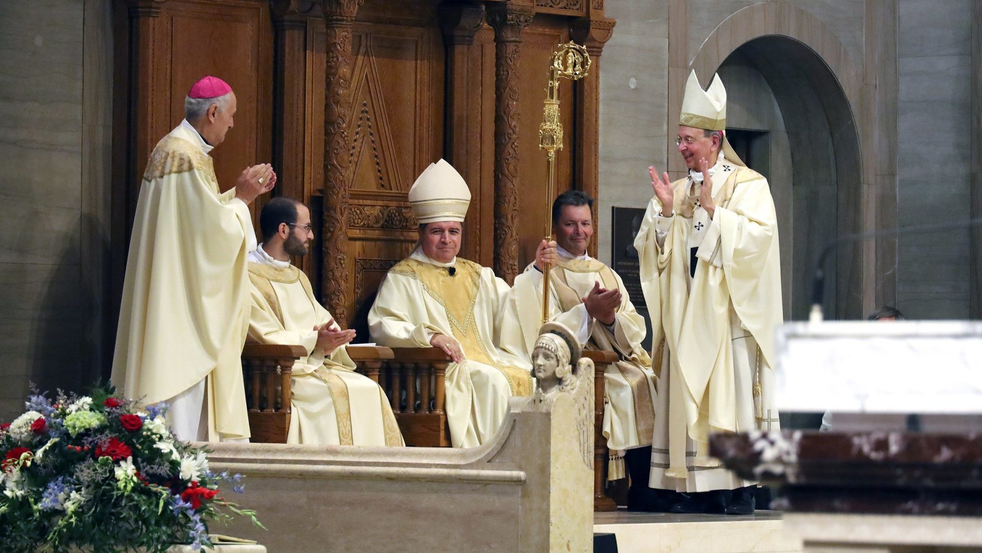 El obispo Evelio Menjívar-Ayala ocupa la cátedra, o silla episcopal, durante su instalación como décimo obispo de Wheeling-Charleston, Virginia Occidental, en julio, en la Catedral de San José de Wheeling. Lo acompañan, de izquierda a derecha, el arzobispo Gabriele G. Caccia, nuncio apostólico en Estados Unidos; el arzobispo William E. Lori, de Baltimore; y miembros del clero, quienes aplauden. (Foto OSV News/Colleen Rowan, The Catholic Spirit)