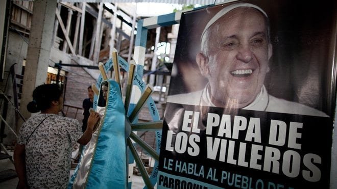 A woman touches a religious figure beside a banner of Pope Francis reading in Spanish
