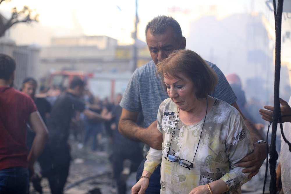 A woman is assisted at the site of a car bomb blast outside the Syriac Orthodox Church of the Blessed Virgin Mary in Qamishli
