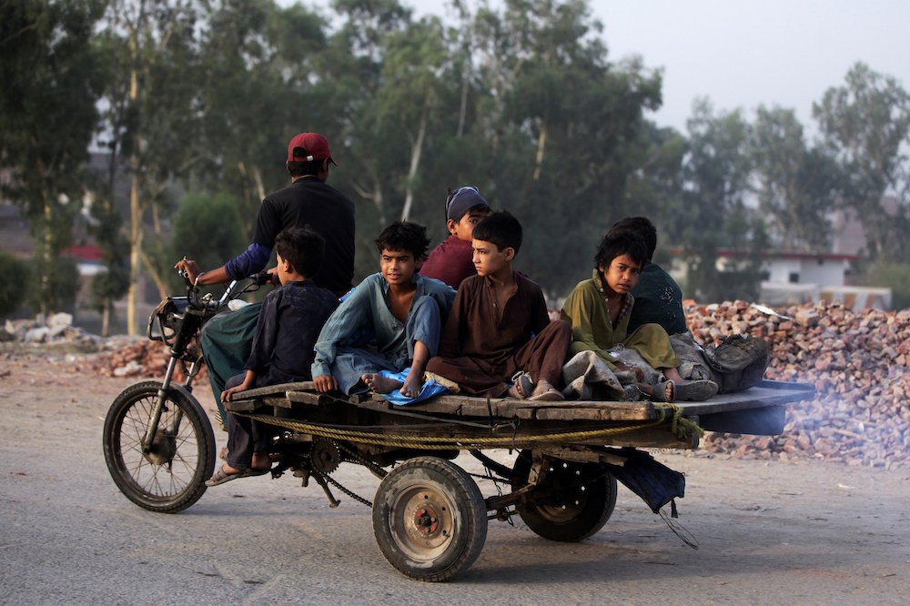 Boys from an Afghan refugee family ride on a motorcycle cart as they head to search for recyclables in Lahore