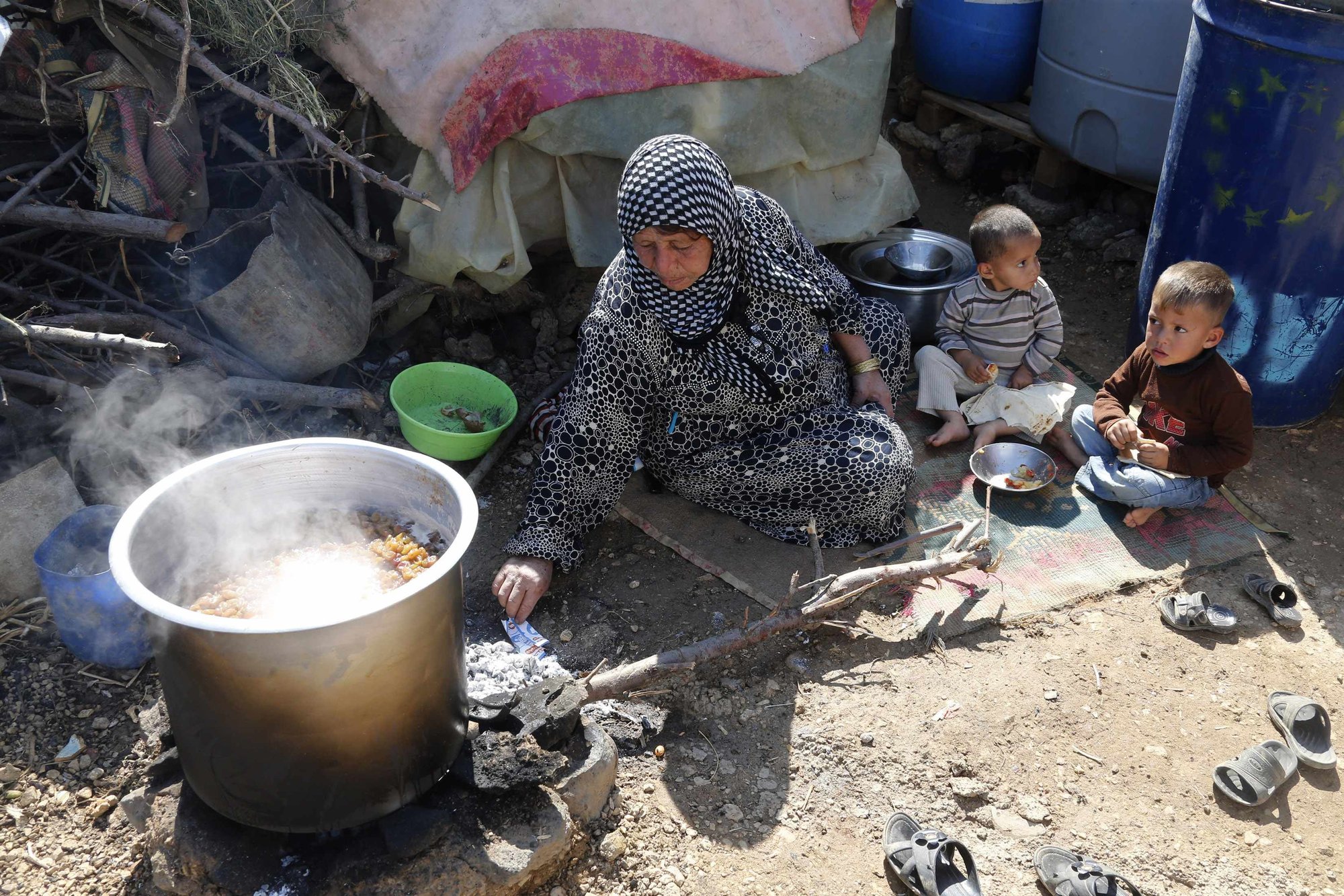 Syrian refugees rest while cooking a meal at an informal settlement in Bekaa