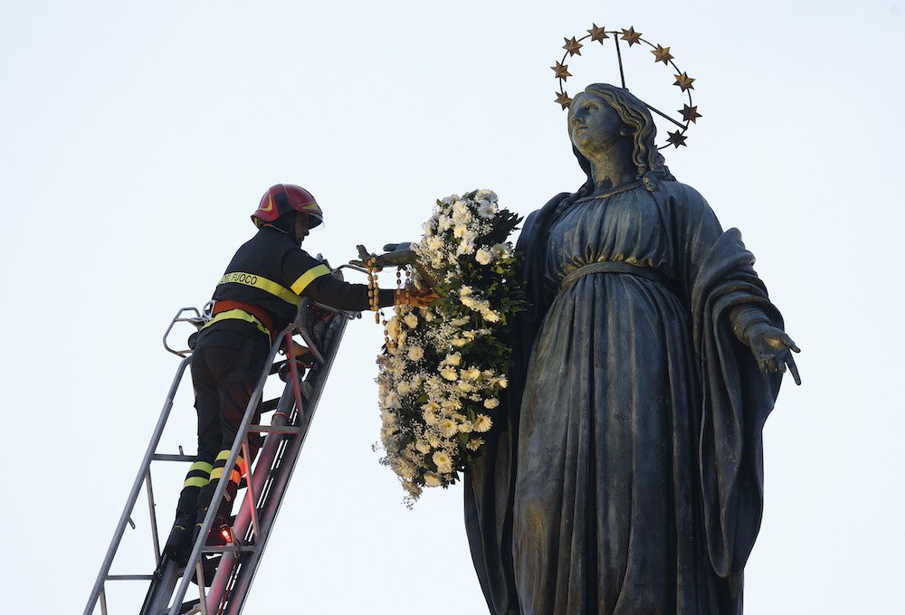 A firefighter places a wreath on a tall statue of Mary overlooking the Spanish Steps in Rome Dec. 8