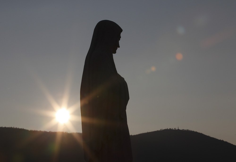The sun sets behind a statue of Mary on Apparition Hill in Medjugorje