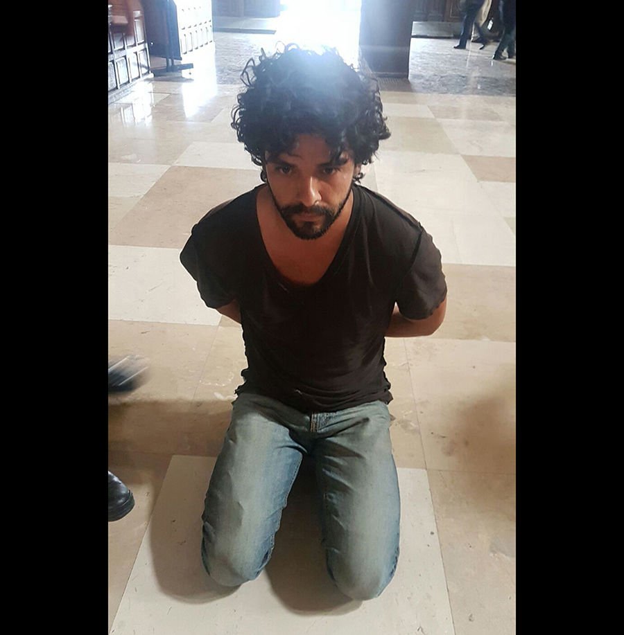 John Rock Schild is seen handcuffed after being accused of stabbing Father Miguel Angel Machorro three times during Mass May 15 at the Metropolitan Cathedral in Mexico City. (CNS photo/EPA)