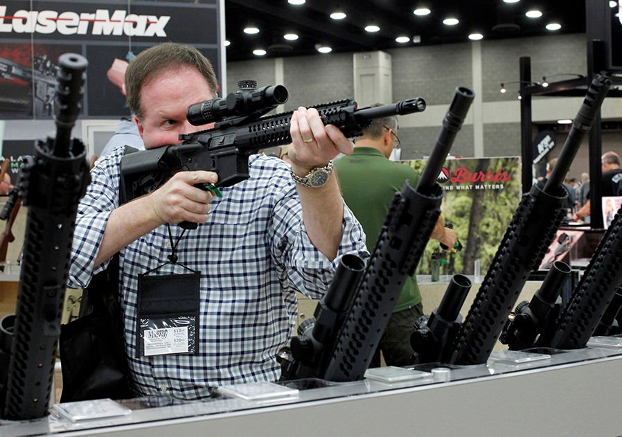 A man looks through a rifle scope at the National Rifle Association’s Annual Meetings and Exhibits show in Louisville