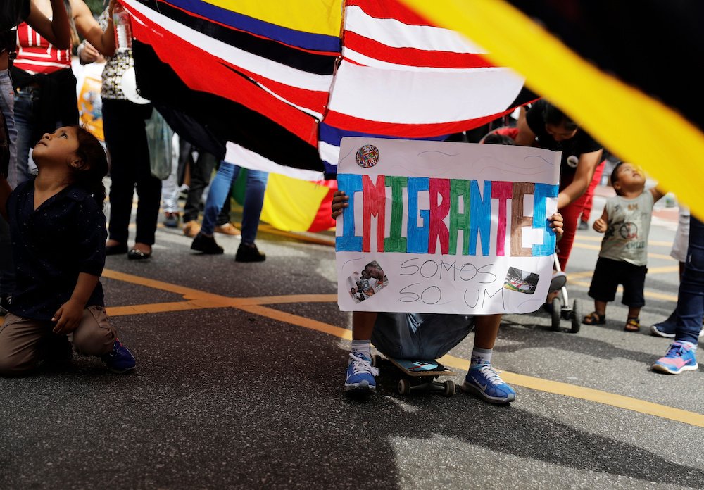 A child holds a sign that reads "Migrants