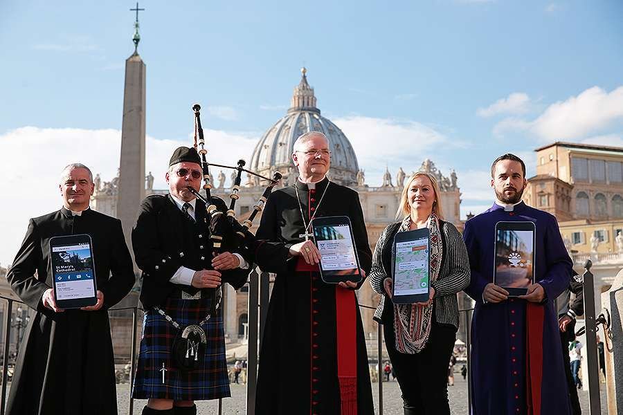 Archbishop Leo Cushley (C) demonstrates The Catholic App in St. Peter's Square