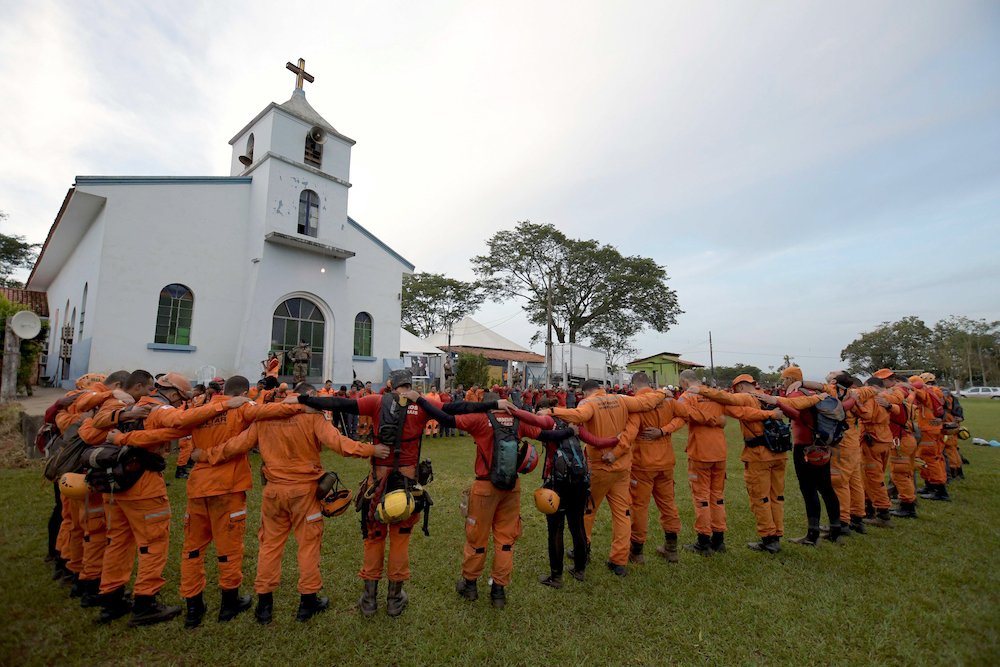 Members of a rescue team pray before working in a collapsed tailings dam owned by mining company in Brumadinho