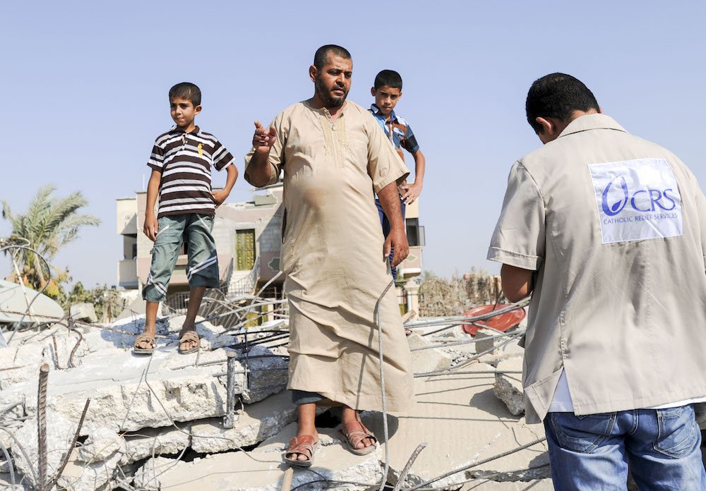 A worker with Catholic Relief Services talks to a man as he stands amid the rubble of his home destroyed during the Gaza-Israeli conflict in 2014. CRS recently cut its services to needy people in the Gaza Strip by closing a U.S. government-funded program because of the Anti-Terrorism Clarification Act. This was the second CRS program in Gaza affected the U.S. government decisions in recent months. (CNS photo/Shareef Sarhan