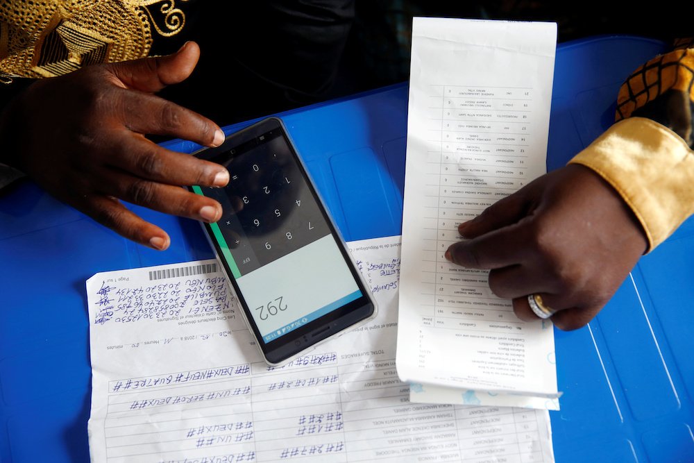 An official of the Congolese Independent National Electoral Commission uses his phone to calculate the numbers of presidential election votes at a tallying center in Kinshasa Jan. 4