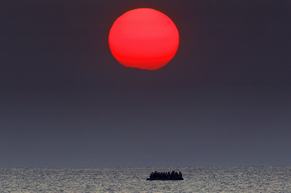 A red sun is seen over a dinghy overcrowded with Syrian refugees drifting in the Aegean sea between Turkey and Greece after its motor broke down off the Greek island of Kos