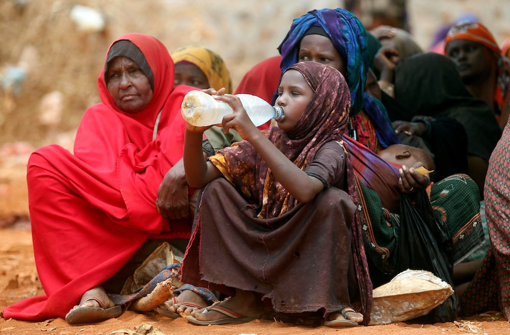 Internally displaced Somali women wait for relief food while a child drinks water April 9