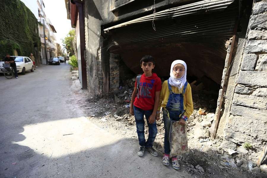 12-year-old twins stand near garbage outside a building in the old city of Homs