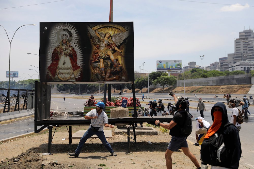 Supporters of Venezuelan opposition leader Juan Guaido throw stones at riot police in front of images of Mary and the Christ Child and Michael the Archangel May 1