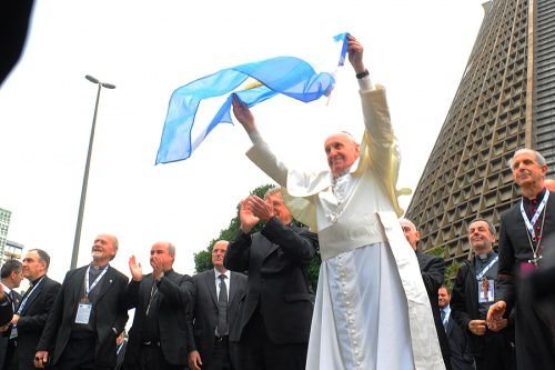Pope Francis waves an Argentine flag during World Youth Day 2013. Credit: Alex Mazzullo/JMJ Rio 2013 via Flickr (CC BY-NC-SA 2.0).