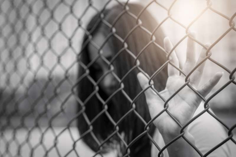 Women raises hand on chain-link fence. Credit: PORNCHAI SODA_Shutterstock