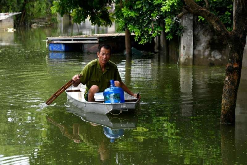 A man rows a boat through floodwaters as he brings potable water back to his flooded home in Hanoi's suburban Chuong My district