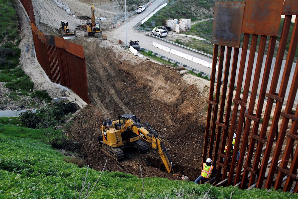 Construction workers in the U.S. work on a new section of the border wall as seen from Tijuana