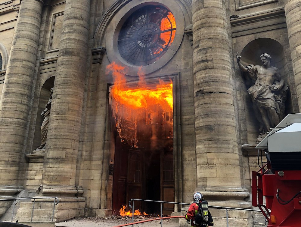 A firefighter is seen as flames shoot through the front door of St. Sulpice Church in Paris March 17