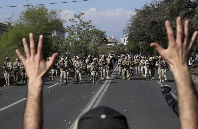 A demonstrator holds up his hands toward advancing soldiers during a protest as a state of emergency remains in effect in Santiago, Chile, Sunday, Oct. 20, 2019. Protests in the country have spilled over into a new day, even after President Sebastian Pinera cancelled the subway fare hike that prompted massive and violent demonstrations. (Esteban Felix/AP via Crux)