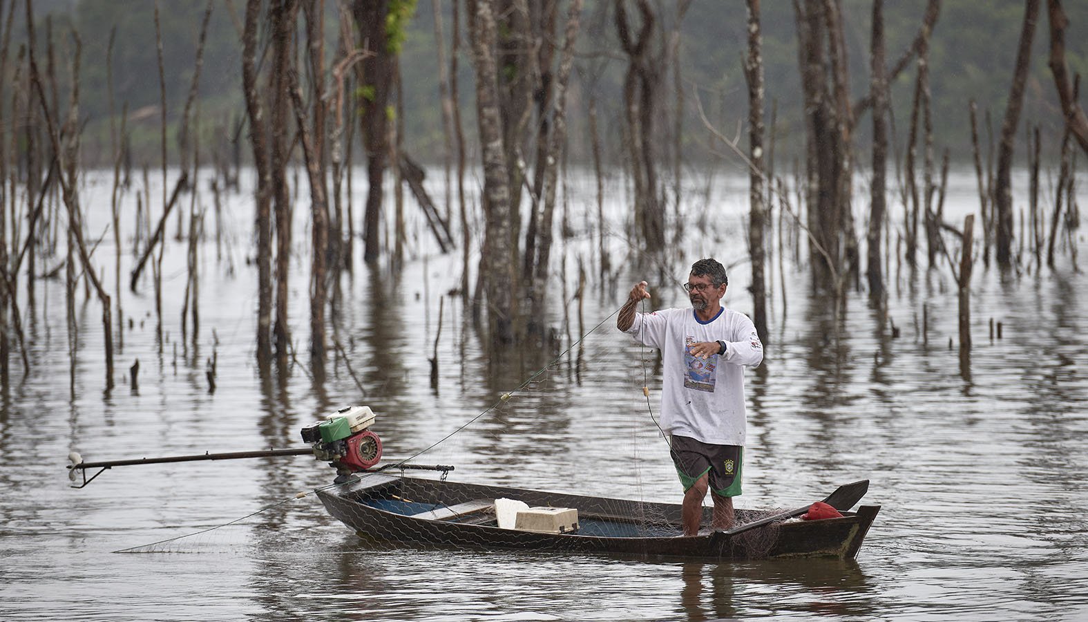 Londolfo Aranha Neto, 59, casts his net among treetops at the edge of the Belo Monte Dam reservoir, near Altamira, Brazil. He is among the thousands of fisher families displaced by the flooding of the Xingu River who are slowly moving back. But the once-rich fishing grounds yield far fewer fish than before, and he says fishers constantly snag their nets on submerged trees. (CNS photo/Paul Jeffrey)