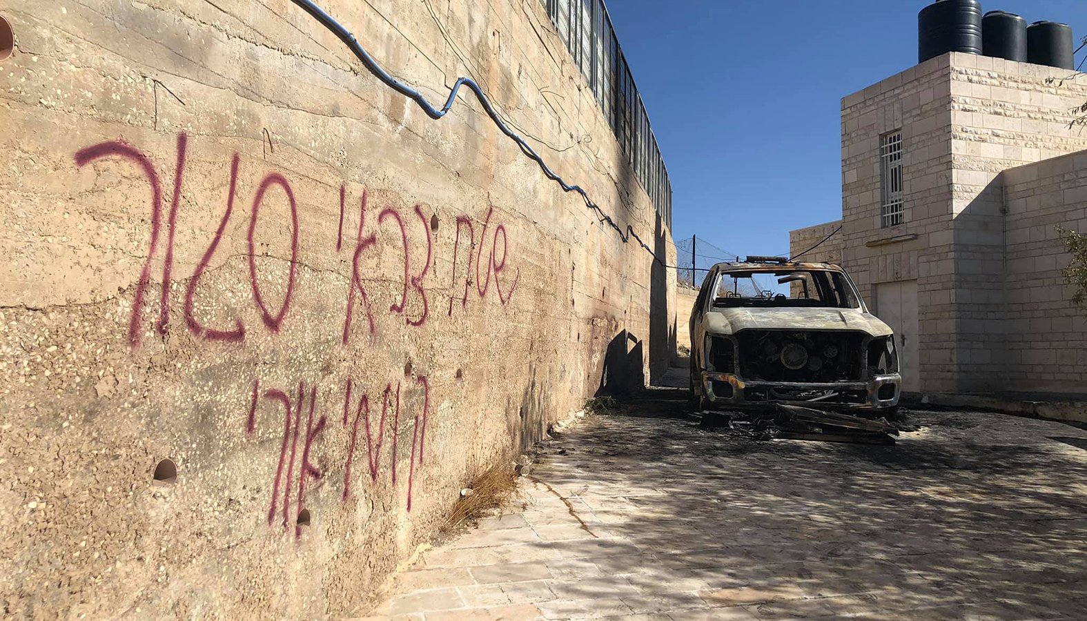 Graffiti is seen in Hebrew on a wall next to a car was burned in the Palestinian town of Taybeh, east of Ramallah, West Bank. The Assembly of Catholic Ordinaries of the Holy Land condemned vandalism attacks in two Arab villages and called on Israeli authorities to "investigate seriously" what they termed hate crimes. (CNS photo/Taybeh Municipality)