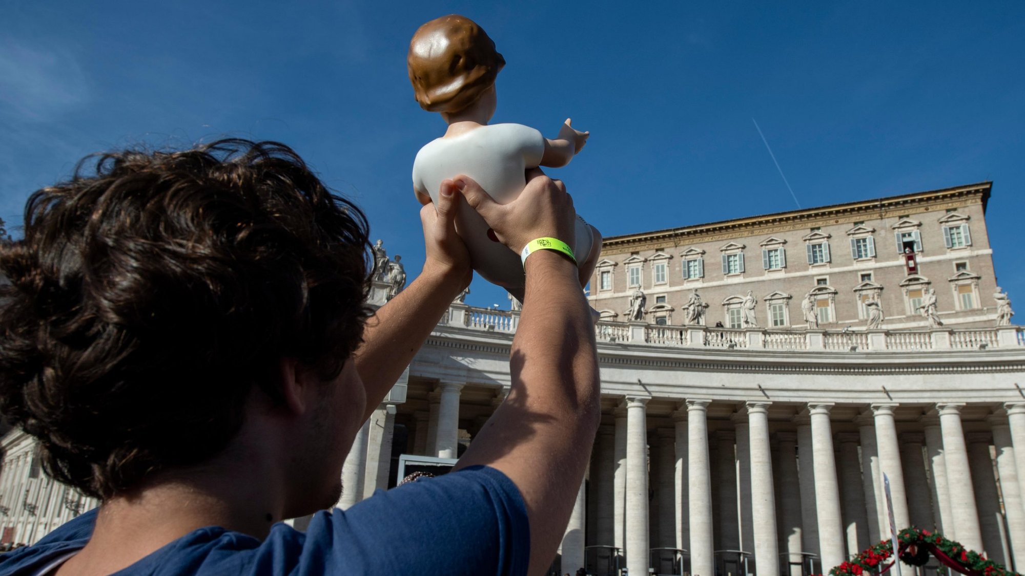 A pilgrim holds up a figurine of the Christ Child as Pope Francis leads the Angelus from the window of his studio overlooking St. Peter's Square at the Vatican Dec 15, 2019. (CNS photo/Vatican Media)