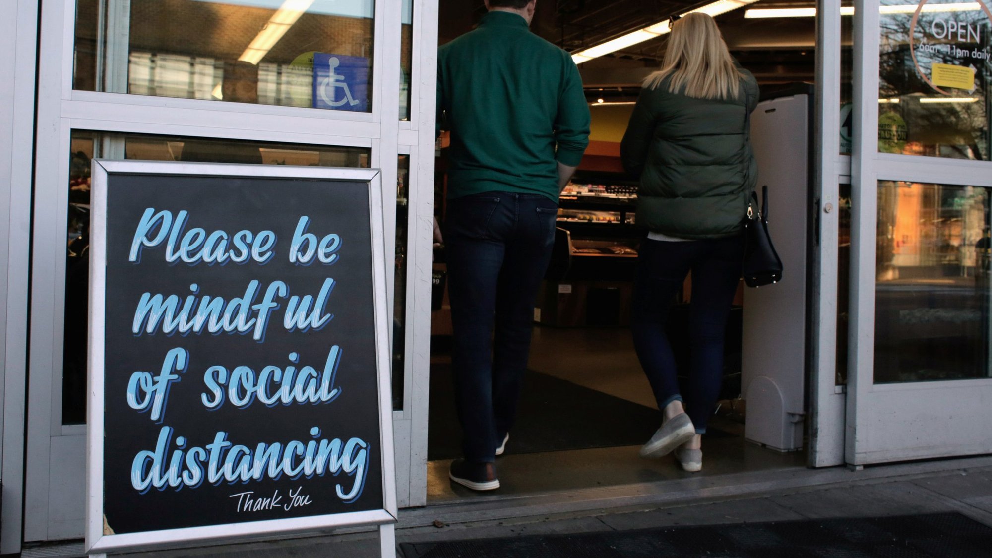 Shoppers enter a Seattle grocery store March 17, 2020, near a sign requesting social distancing, following reports of coronavirus cases in the area. (CNS photo/David Ryder, Reuters)