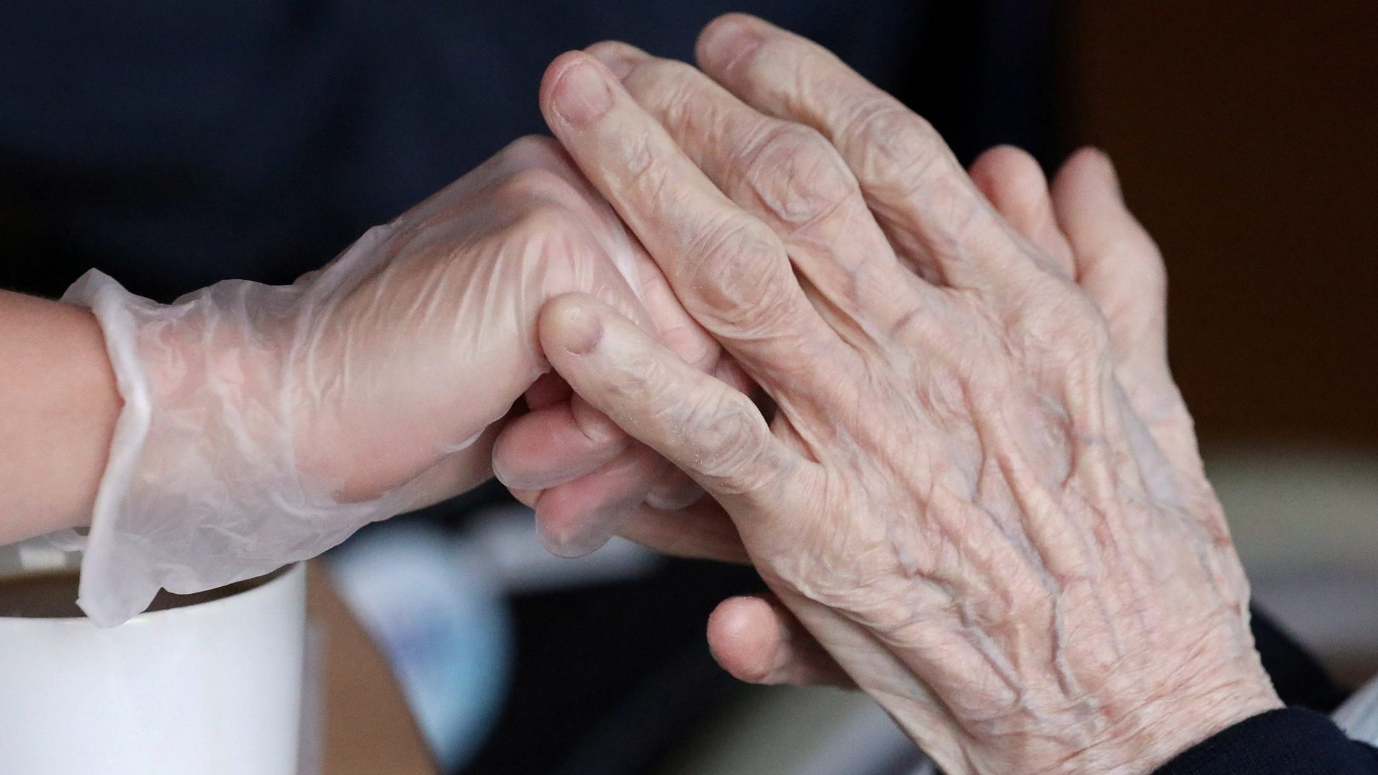 An employee holds the hand of a person at an elderly residence in Brussels April 14, 2020, during the COVID-19 pandemic. During his April 15 morning Mass at the Vatican, Pope Francis prayed for the elderly who are fearful of dying alone during the pandemic. (CNS photo/Yves Herman, Reuters)