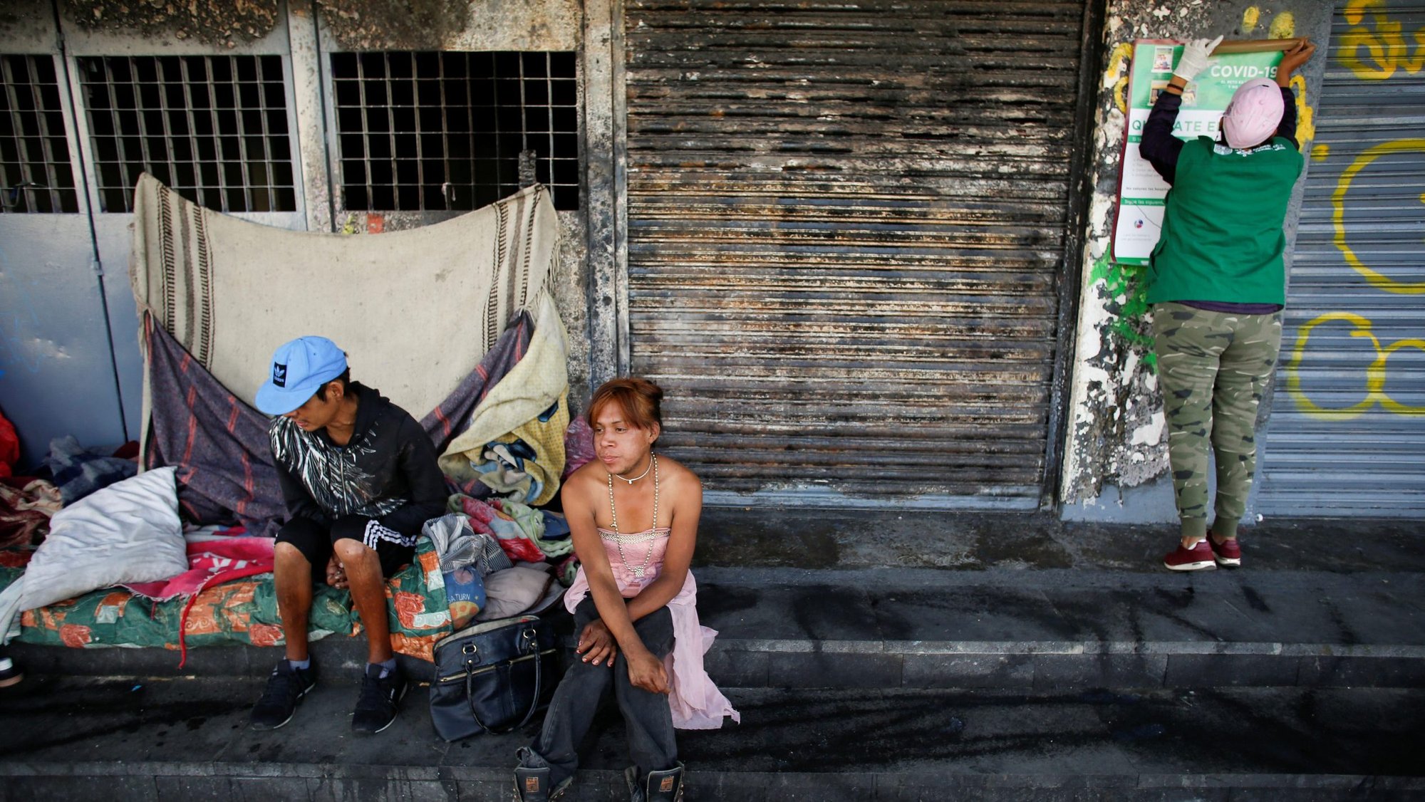 A city government worker places a poster with information next to homeless people in Mexico City March 31, 2020, during the COVID-19 pandemic. (CNS photo/Gustavo Graf, Reuters)