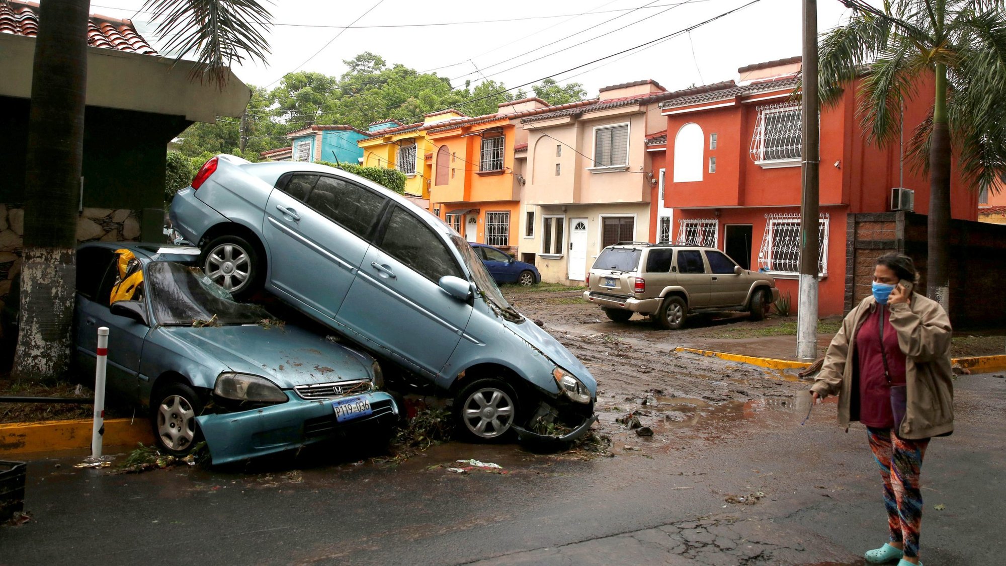A woman wearing a protective mask walks past damaged cars in San Salvador, El Salvador, May 31, 2020, after Tropical Storm Amanda swept through the area. (CNS photo/Jose Cabezas, Reuters)