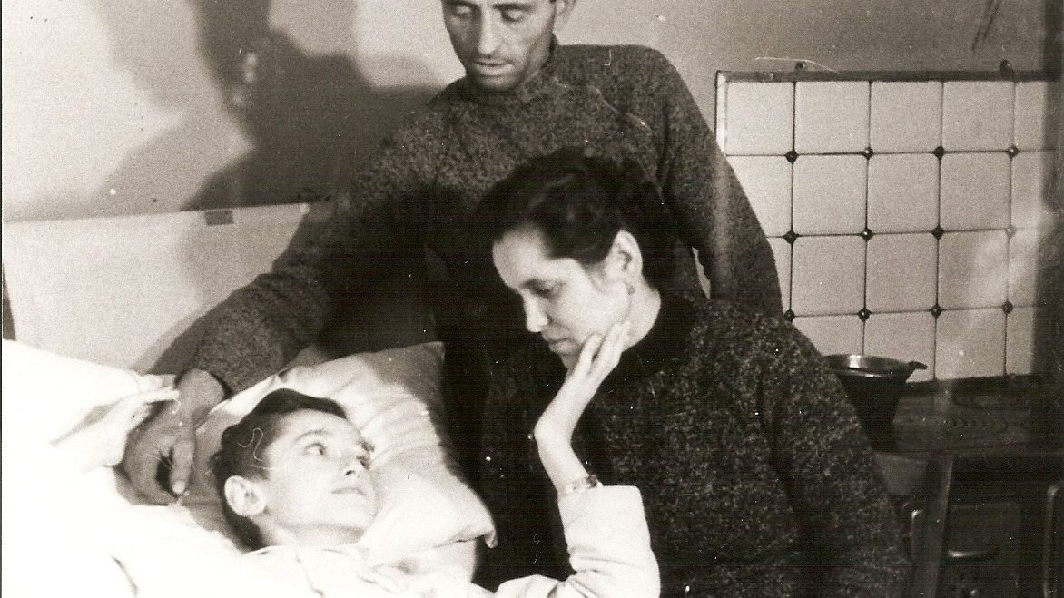 Angiolino Bonetta lying in bed, with his parents beside him. (Image via Facebook @servodidioangiolinobonetta)